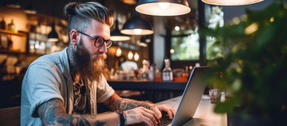 A hipster-looking guy making money from his laptop at a coffee shop.