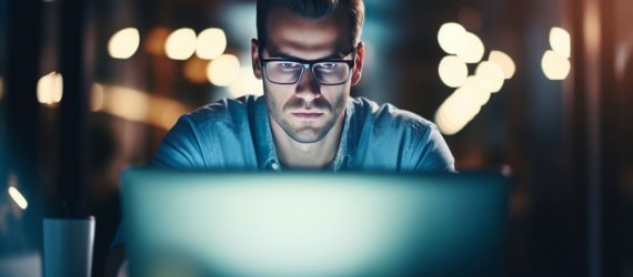 A man with glasses browsing through different online business ideas on his laptop.